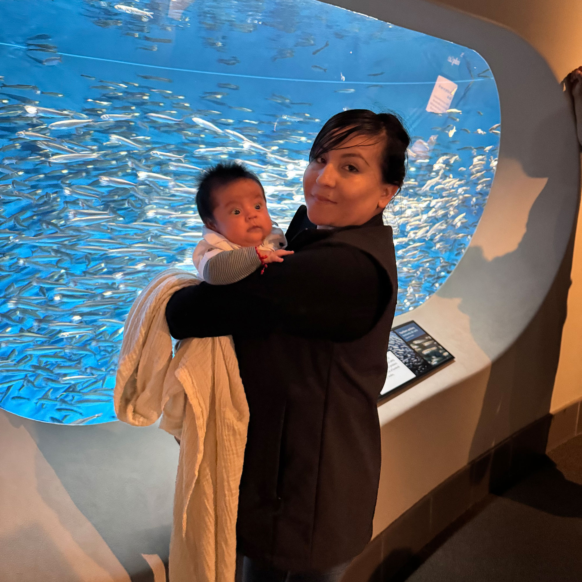 Karla holding baby Gael beside a blue aquarium filled with fish.