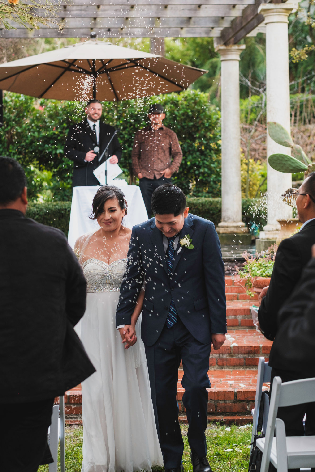 Karla and Birhon walking hand in hand as guests celebrate after their wedding ceremony.
