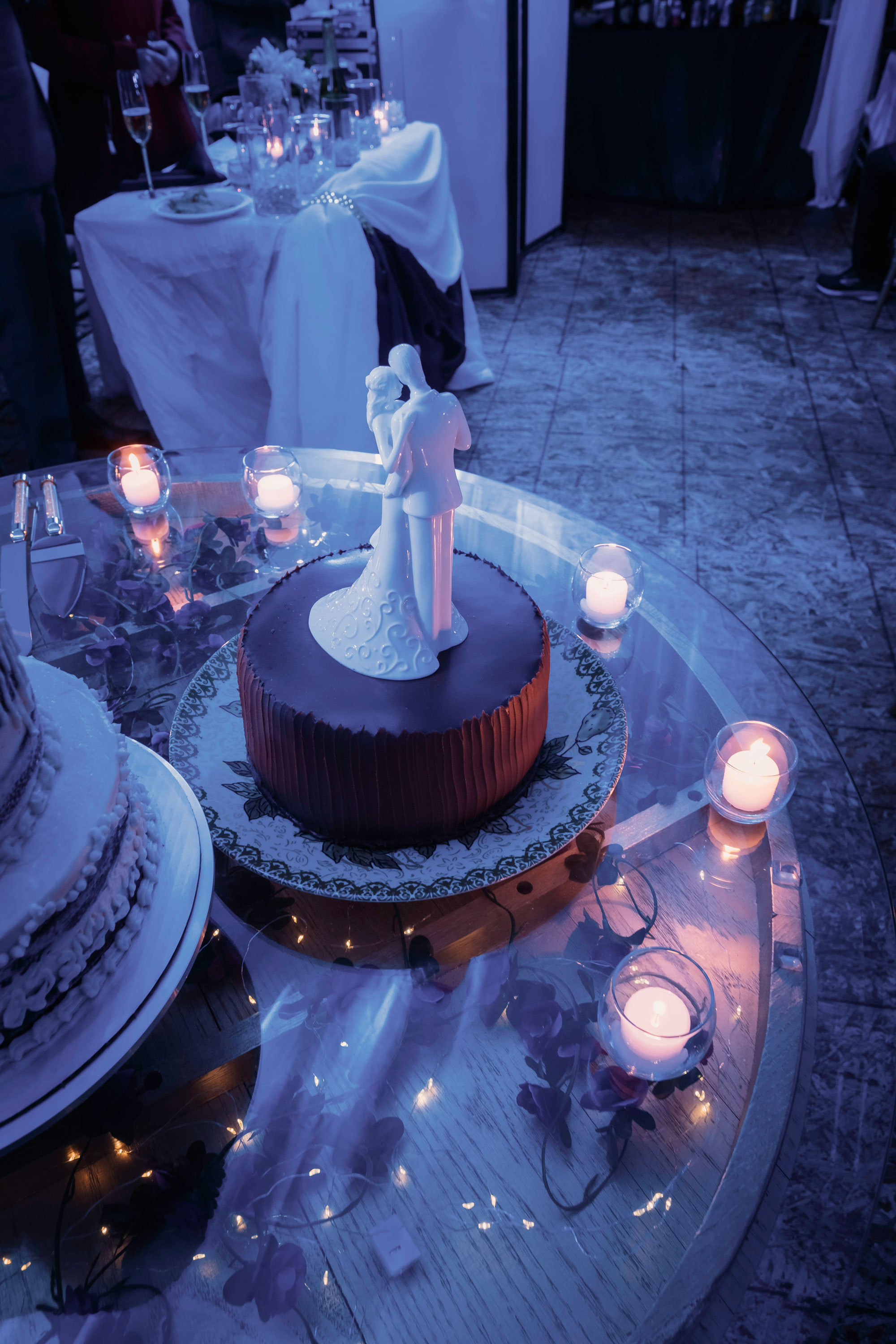 Wedding cake with a bride-and-groom topper surrounded by glowing candles.